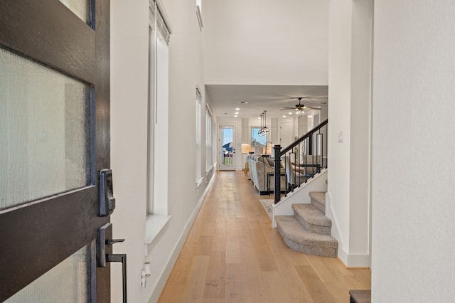 foyer featuring a ceiling fan, a high ceiling, stairway, baseboards, and light wood-style floors