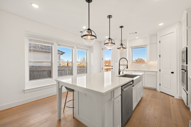 kitchen with sink, white cabinets, pendant lighting, stainless steel appliances, and a center island with sink