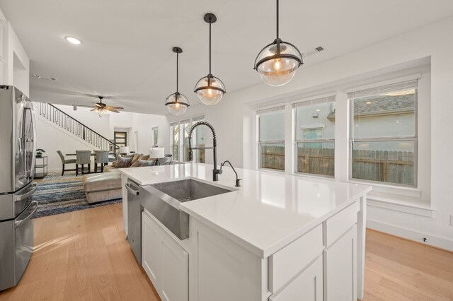 kitchen with white cabinets, appliances with stainless steel finishes, decorative light fixtures, light hardwood / wood-style floors, and a center island with sink