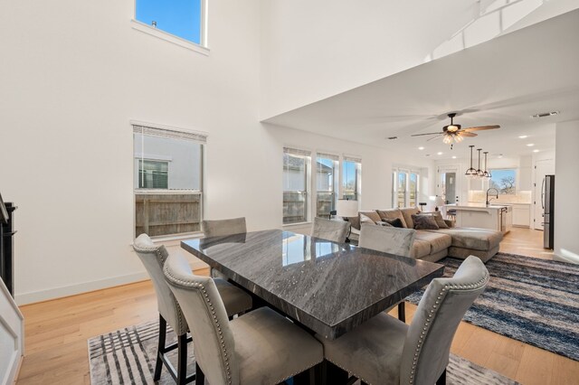 dining space featuring ceiling fan, sink, light hardwood / wood-style flooring, and a towering ceiling