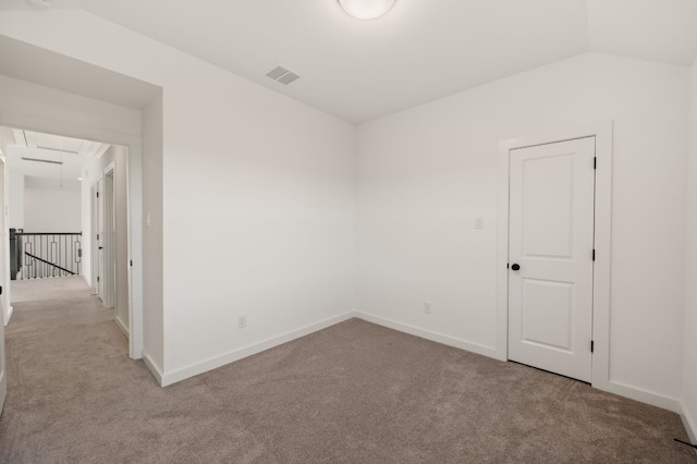 carpeted spare room with baseboards, lofted ceiling, visible vents, and attic access