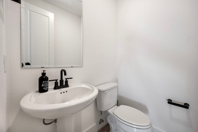 half bathroom with toilet, baseboards, and a sink