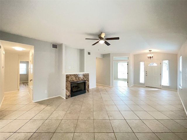 unfurnished living room with ceiling fan with notable chandelier, vaulted ceiling, light tile patterned floors, and a wealth of natural light