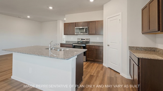 kitchen with light stone counters, sink, stainless steel appliances, and a kitchen island with sink