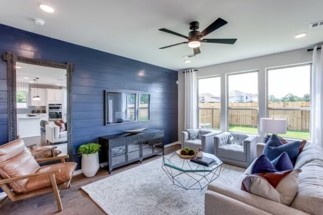 living room with ceiling fan, wood walls, and wood-type flooring