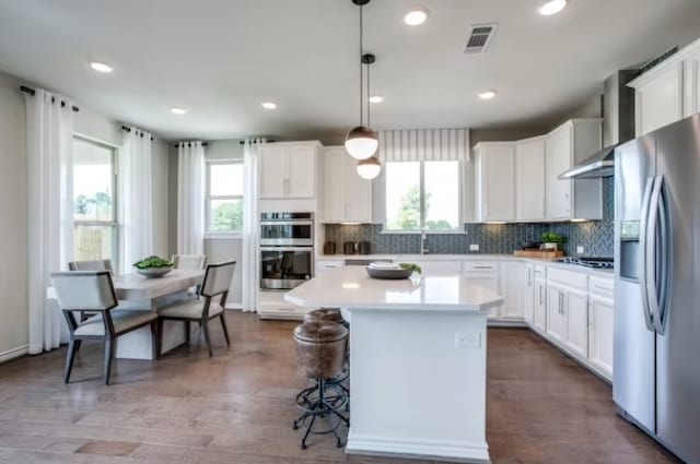 kitchen featuring decorative light fixtures, stainless steel appliances, a center island, and white cabinetry