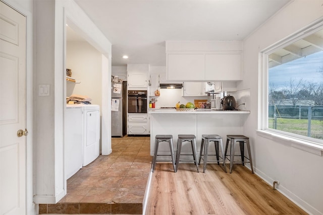 kitchen featuring kitchen peninsula, black oven, washing machine and dryer, white cabinets, and a kitchen breakfast bar