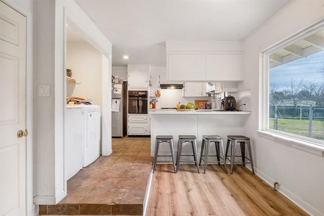 504 Marburger St, Smithville, TX 78957 - kitchen featuring washing machine and dryer, black oven, a peninsula, white cabinets, and a breakfast bar