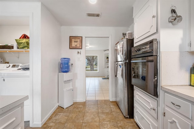 kitchen with light tile patterned floors, stainless steel refrigerator, wall oven, white cabinets, and washer / dryer