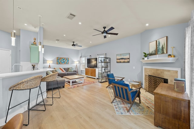 living room featuring a fireplace, ceiling fan, and light hardwood / wood-style floors