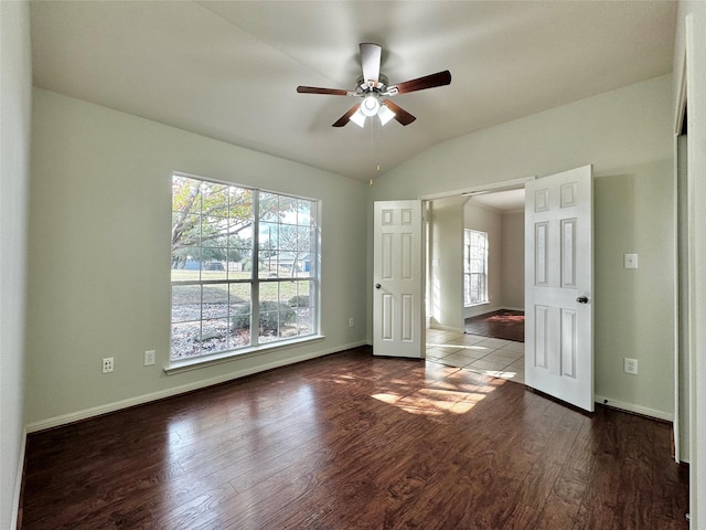 empty room featuring lofted ceiling, ceiling fan, a wealth of natural light, and dark hardwood / wood-style floors