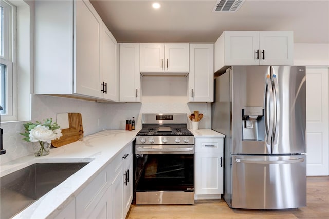 kitchen featuring light stone countertops, white cabinets, light hardwood / wood-style floors, and appliances with stainless steel finishes