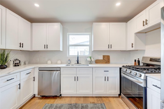 kitchen with stainless steel appliances, light wood-type flooring, light stone counters, sink, and white cabinetry