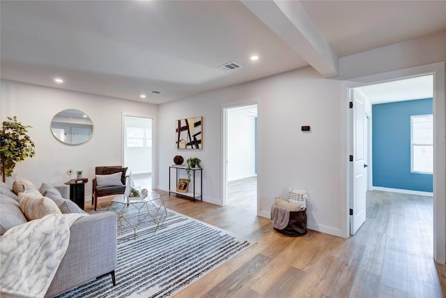 living room with beam ceiling, light wood-type flooring, and plenty of natural light