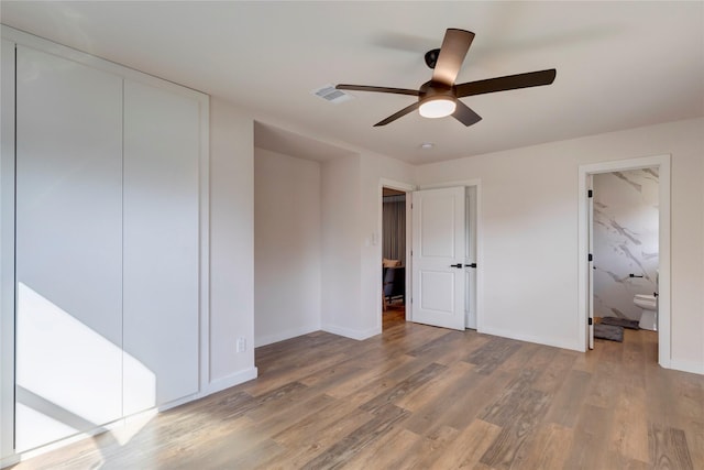 unfurnished bedroom featuring ceiling fan, connected bathroom, a closet, and wood-type flooring