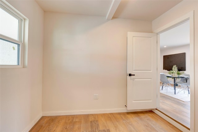 spare room featuring light wood-type flooring and beamed ceiling