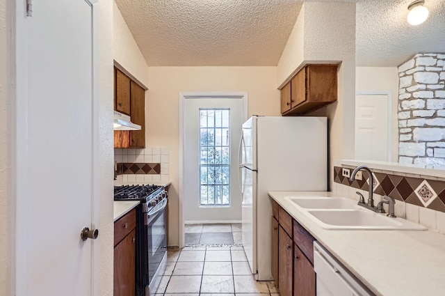 kitchen featuring white appliances, a textured ceiling, light tile patterned floors, backsplash, and sink