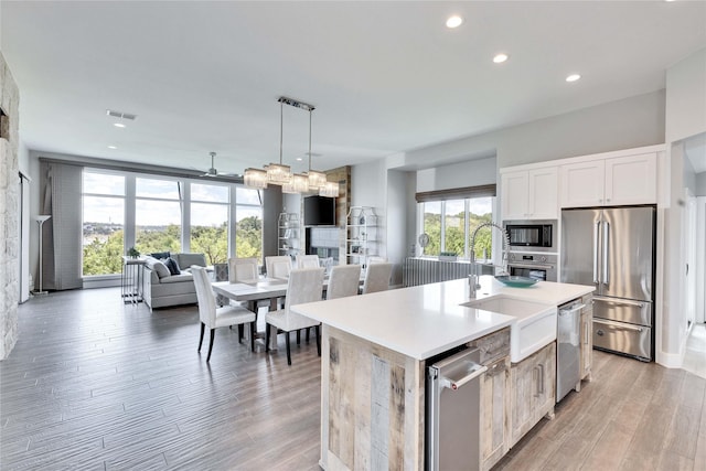 kitchen with pendant lighting, stainless steel appliances, a kitchen island with sink, white cabinets, and ceiling fan