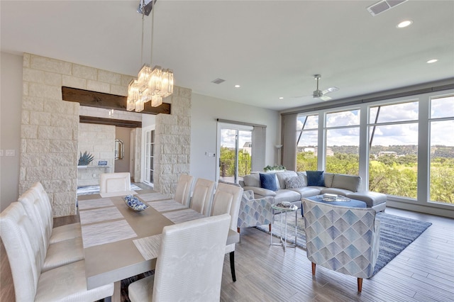 dining area with ceiling fan with notable chandelier, a fireplace, and light hardwood / wood-style floors