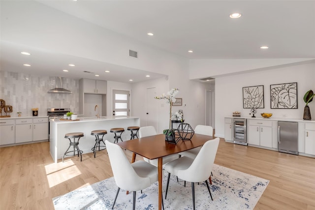 dining space with lofted ceiling, beverage cooler, light hardwood / wood-style floors, and sink