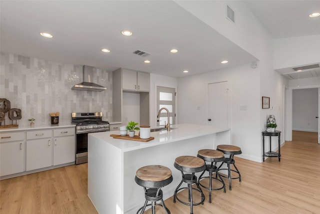 kitchen with stainless steel gas range, wall chimney exhaust hood, a kitchen bar, backsplash, and sink