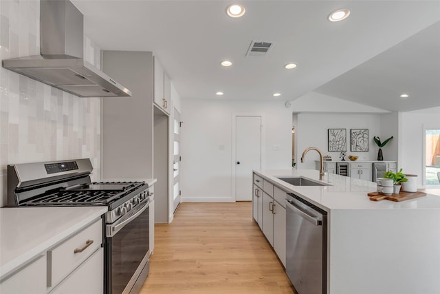 kitchen featuring a kitchen island with sink, appliances with stainless steel finishes, sink, white cabinetry, and wall chimney range hood