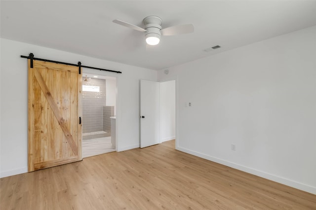 unfurnished bedroom with ensuite bathroom, ceiling fan, a barn door, and hardwood / wood-style floors