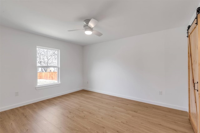 unfurnished room with ceiling fan, a barn door, and light hardwood / wood-style flooring