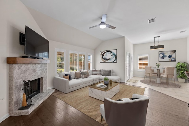 living room featuring vaulted ceiling, ceiling fan, wood-type flooring, and a stone fireplace