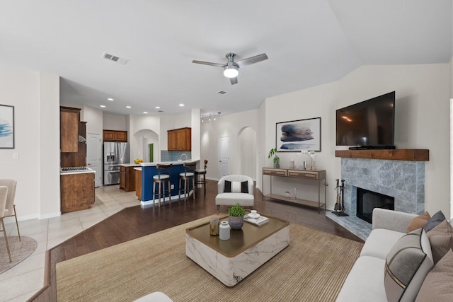 tiled living room with vaulted ceiling, a fireplace, and ceiling fan