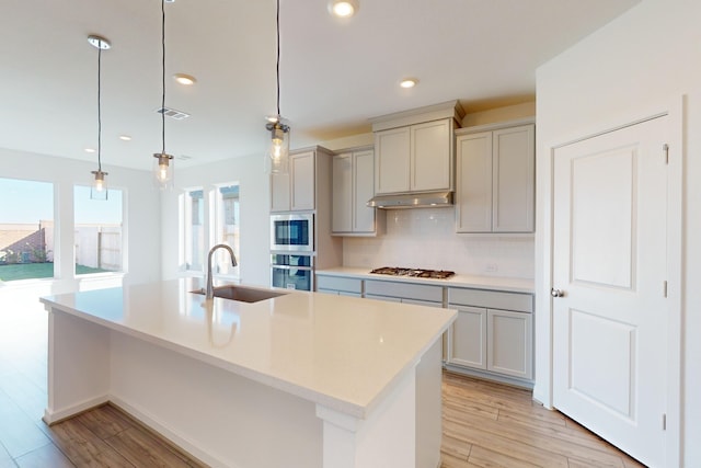 kitchen featuring stainless steel appliances, a kitchen island with sink, gray cabinetry, and sink