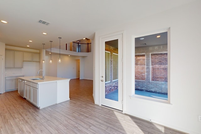 kitchen featuring light hardwood / wood-style flooring, pendant lighting, a center island with sink, decorative backsplash, and sink