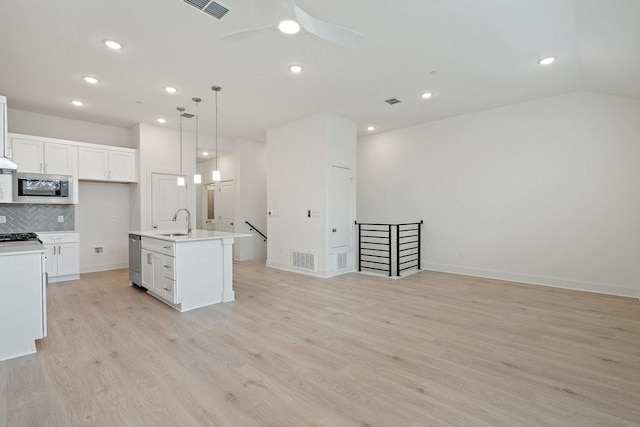 kitchen with decorative light fixtures, an island with sink, tasteful backsplash, white cabinetry, and sink