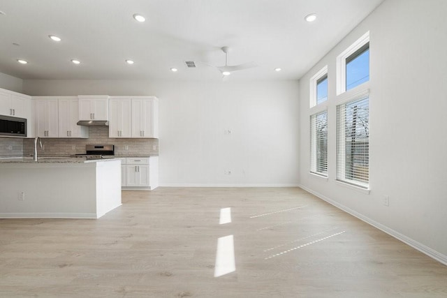 kitchen featuring white cabinetry, stainless steel appliances, light stone countertops, light hardwood / wood-style floors, and backsplash