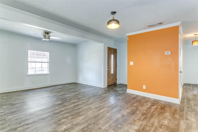 empty room with a textured ceiling, ceiling fan, ornamental molding, and wood-type flooring