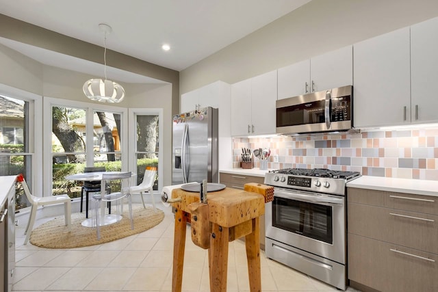 kitchen featuring decorative light fixtures, stainless steel appliances, decorative backsplash, white cabinets, and light tile patterned flooring