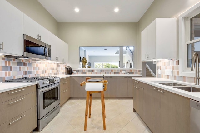 kitchen with sink, light tile patterned flooring, tasteful backsplash, and appliances with stainless steel finishes