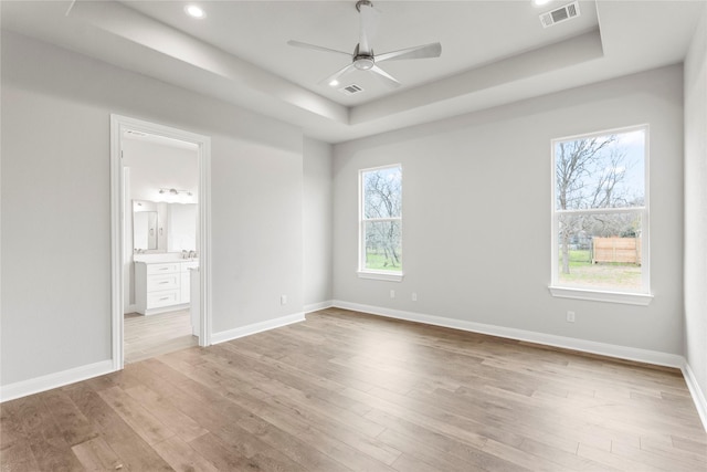 empty room with ceiling fan, a tray ceiling, and light hardwood / wood-style flooring