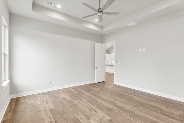 empty room with ceiling fan, a tray ceiling, and light hardwood / wood-style floors