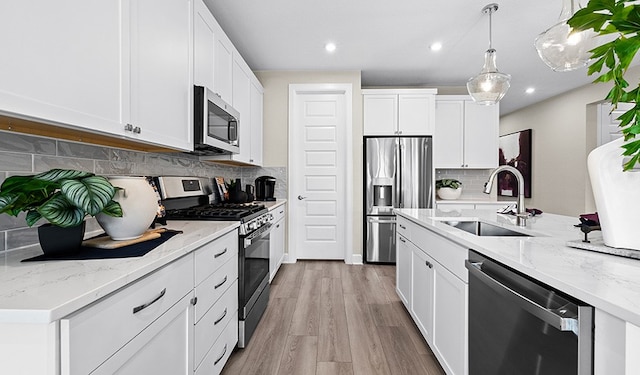 kitchen with sink, white cabinetry, light stone counters, appliances with stainless steel finishes, and pendant lighting