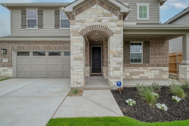 16904 Astral Ln, Manor, TX 78653 - doorway to property featuring driveway, stone siding, an attached garage, and brick siding