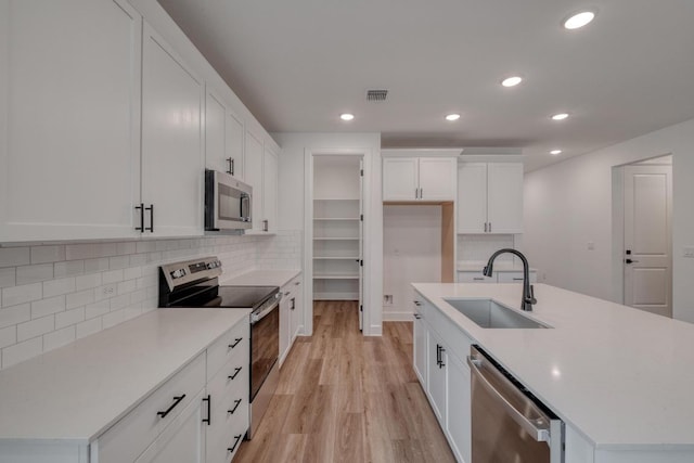16904 Astral Ln, Manor, TX 78653 - kitchen featuring appliances with stainless steel finishes, light wood-style flooring, recessed lighting, white cabinets, and an island with sink