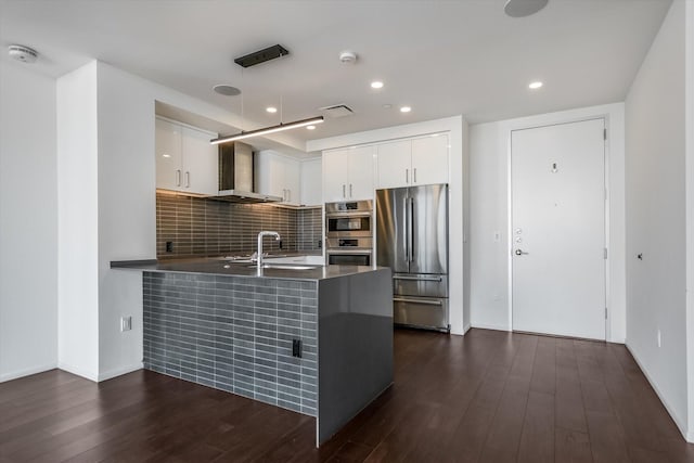 kitchen with stainless steel appliances, white cabinetry, kitchen peninsula, and wall chimney exhaust hood