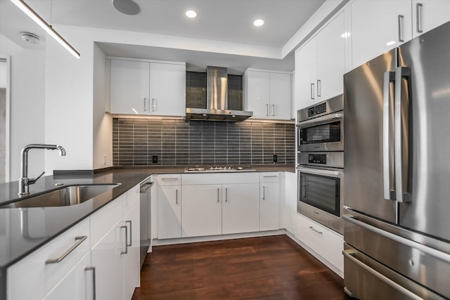 kitchen with appliances with stainless steel finishes, white cabinets, sink, and wall chimney exhaust hood