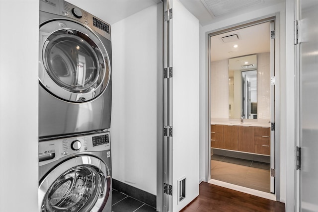 clothes washing area featuring stacked washing maching and dryer, dark hardwood / wood-style floors, and sink