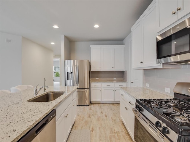 kitchen featuring stainless steel appliances, white cabinetry, backsplash, and light stone counters