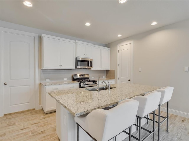 kitchen featuring a kitchen island with sink, stainless steel appliances, light stone counters, sink, and white cabinetry