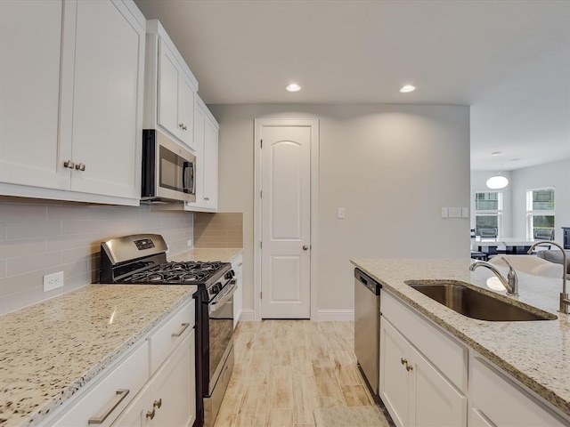 kitchen featuring stainless steel appliances, white cabinets, sink, and light stone countertops