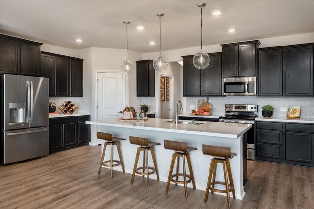 kitchen with stainless steel appliances, an island with sink, sink, decorative light fixtures, and tasteful backsplash