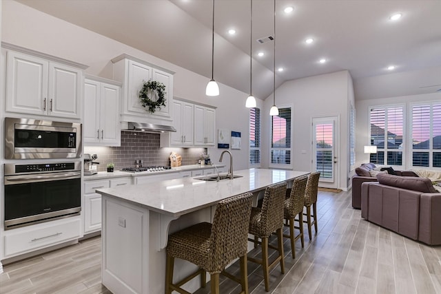 kitchen with vaulted ceiling, a center island with sink, stainless steel appliances, light stone countertops, and sink